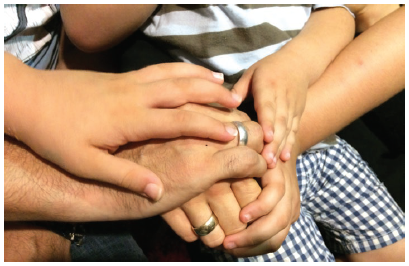 A journalist, his wife, and his three children clasp hands. Now settled in a one-bedroom Air BnB in Athens, they are trying to put their lives back together while worrying about family members they had to leave behind in Turkey.  (Photo: Jennifer Campbell)