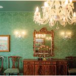 On the opposite side of the grand hall is the expansive dining room with three chandeliers, deep-green patterned wallpaper, a candelabra and a couple of small, carved wooden jewelry boxes on a sideboard. (Photo: Ashley Fraser)
