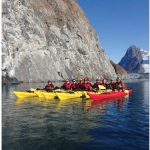 Kayakers line up in formation for a photo break from exploring along cliffs, icebergs and the hanging glaciers high above the ocean in southern Greenland in Kangerlussuatsiaq Fjord. (Photo: Mike Beedell)