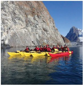 Kayakers line up in formation for  a photo break from exploring along cliffs, icebergs and the hanging glaciers high above the ocean in southern Greenland in Kangerlussuatsiaq Fjord. (Photo: Mike Beedell)