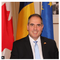 To mark Romania’s national day, the blue, yellow and red flag flew in front of City Hall and Niagara Falls was illuminated in the same colours on Dec. 1. Romanian Ambassador Bogdan Manoiu stands in front of the flags. (Photo: Ülle Baum) 